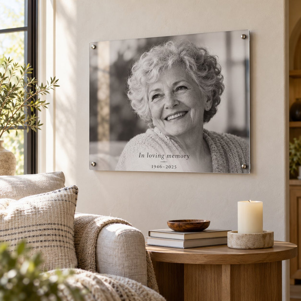 Black and white in loving memory acrylic photo print of a smiling grandmother with the dates 1946–2025, hung in a living room