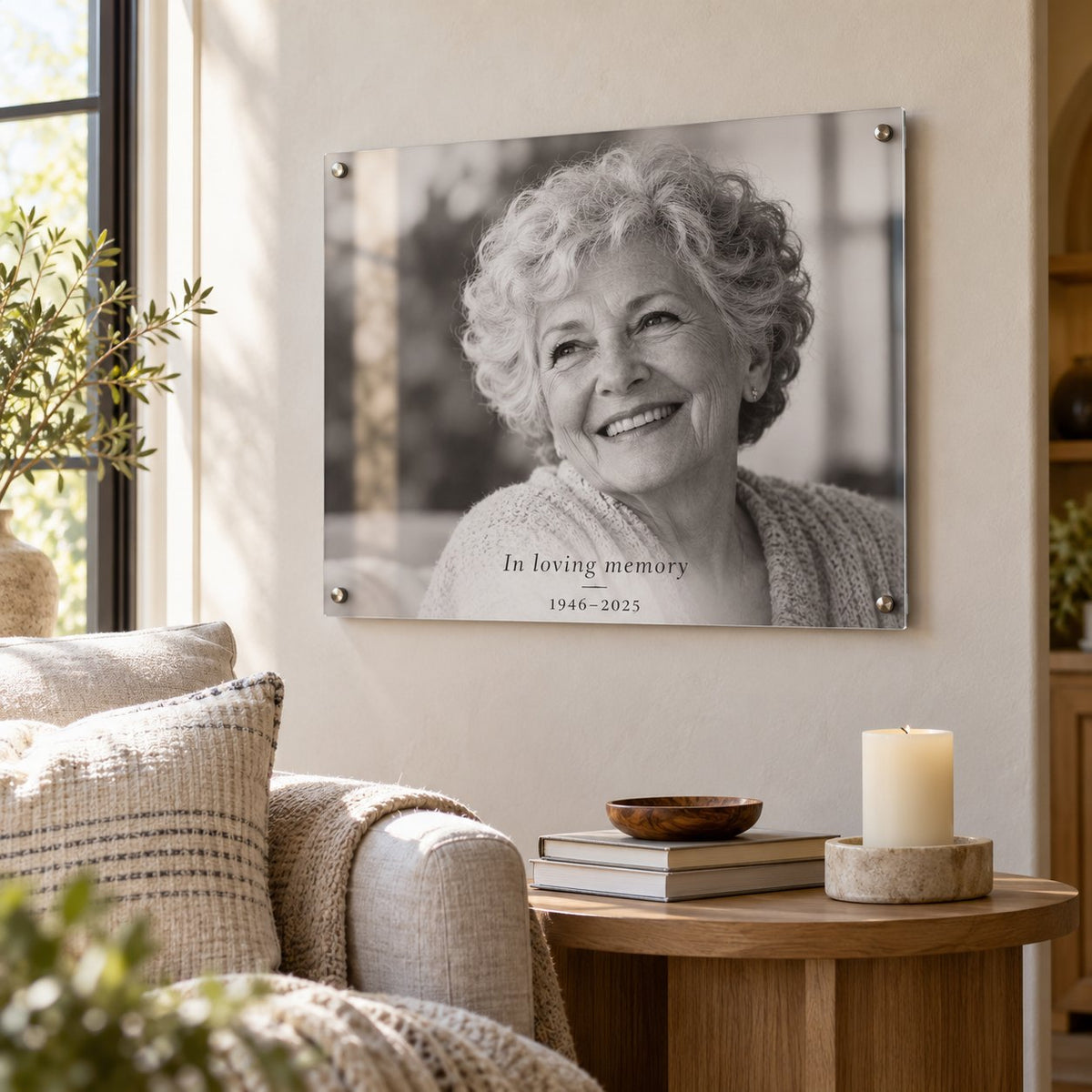 Black and white in loving memory acrylic photo print of a smiling grandmother with the dates 1946–2025, hung in a living room
