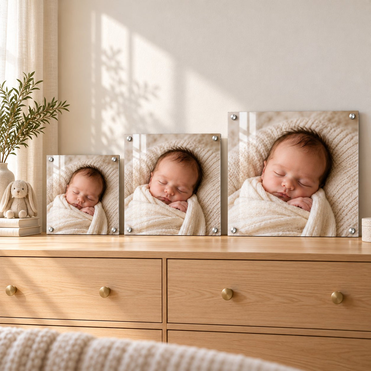 Three newborn photo acrylic prints in small, medium, and large sizes leaning on a nursery dresser to compare sizes