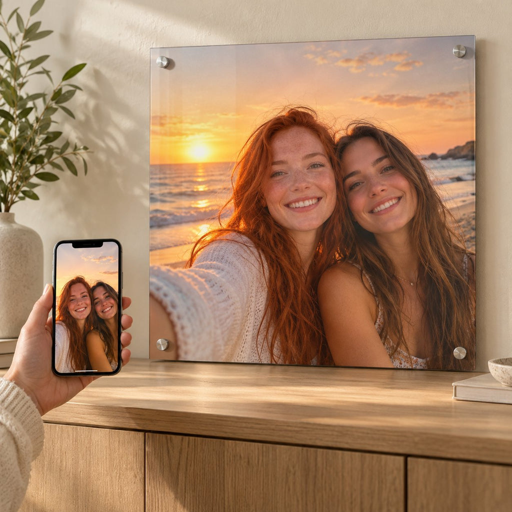 Phone held in front of a large acrylic print of the same beach sunset selfie, showing a phone photo turned into wall art