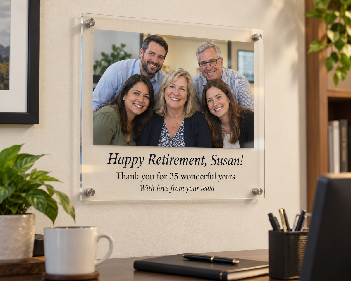 Retirement gift plaque on clear acrylic with a team photo and the message Happy Retirement, Susan! Thank you for 25 wonderful years, hung on an office wall